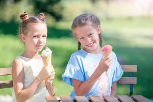 Little girls eating ice-cream outdoors at summer in outdoor cafe photo