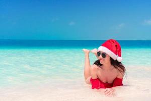 Young happy woman in Santa hat in swimsuit on white beach on Xmas holidays photo