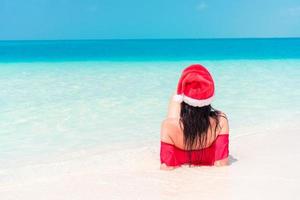 Young happy woman in Santa hat in swimsuit on white beach on Xmas holidays photo