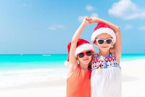 Little adorable girls in Santa hats during beach vacation have fun together photo