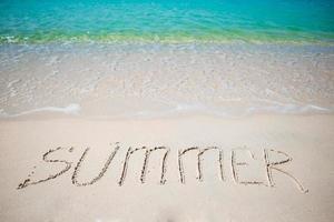 Word Summer handwritten on sandy beach with soft ocean wave on background photo