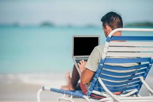 Young man with tablet computer during tropical beach vacation photo