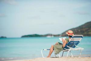 Young woman reading book on chaise-lounge on the beach photo