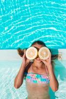 Little girl covering eyes with lemon halves near eyes on background swimming pool photo