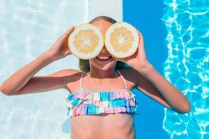 Little girl covering eyes with lemon halves near eyes on background swimming pool photo