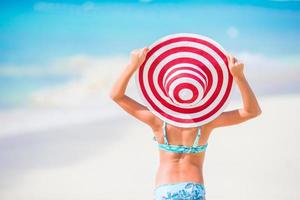 Adorable little girl in big red hat walking along white sand Caribbean beach photo