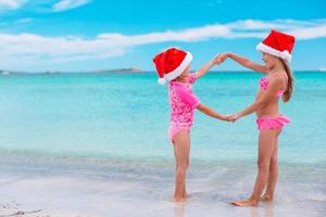 Little adorable girls in Santa hats during beach Christmas vacation having fun together photo