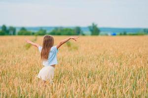 Happy little girl walking in golden fields of wheat photo