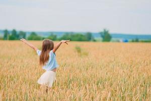 Happy little girl walking in golden fields of wheat photo