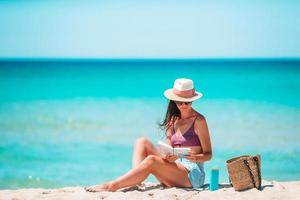 Young woman reading book during tropical white beach photo