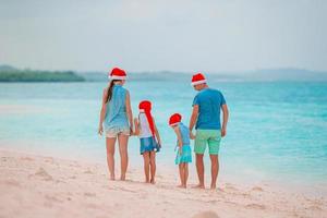 Happy family in red Santa hats on a tropical beach celebrating Christmas vacation photo