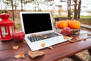 calabaza naranja y hojas cerca de la computadora portátil en una mesa. tiempo de la temporada de otoño foto