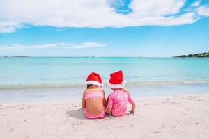 niñas adorables con sombreros de santa durante las vacaciones en la playa se divierten juntas foto