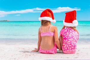 niñas adorables con sombreros de santa durante las vacaciones en la playa se divierten juntas foto