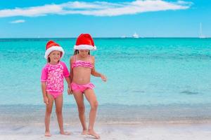 Little adorable girls in Santa hats during beach vacation have fun together photo