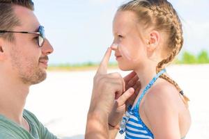 Parent applying sun cream to kid nose. Portrait of cute girl in suncream photo