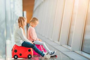 Adorable little girls having fun in airport sitting on suitcase waiting for boarding photo