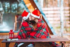 Young family in santa hat sitting on the wooden old table background of their house photo