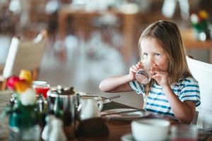 Adorable little girl having breakfast at outdoor cafe photo