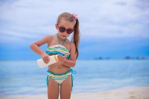 Little adorable girl in swimsuit holds suntan lotion bottle photo