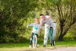 Young father and little girl biking at summer warm day. Young active family ride on bicycles photo