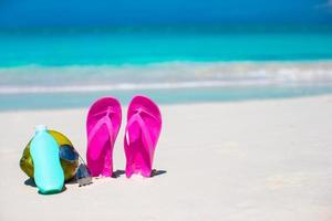 Flip flops, coconut and suncream on white sand. Beach accessories. photo