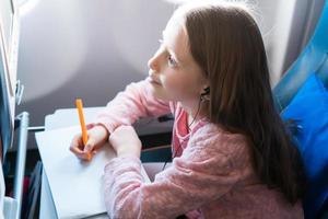 Adorable little girl traveling by an airplane. Kid drawing picture with colorful pencils sitting near window photo