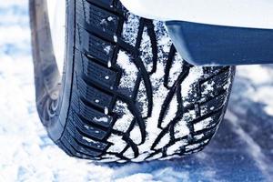 Closeup shot of automobile studded tire covered with snow at winter snowy road photo