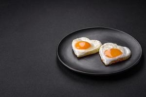 Two heart-shaped fried eggs on a black ceramic plate on a dark concrete background photo