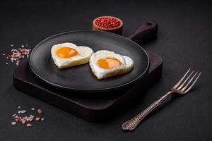 Two heart-shaped fried eggs on a black ceramic plate on a dark concrete background photo