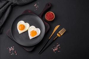 Two heart-shaped fried eggs on a black ceramic plate on a dark concrete background