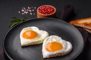 Two heart-shaped fried eggs on a black ceramic plate on a dark concrete background photo