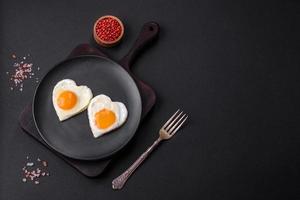 Two heart-shaped fried eggs on a black ceramic plate on a dark concrete background photo
