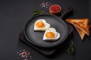 Two heart-shaped fried eggs on a black ceramic plate on a dark concrete background