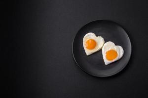 Two heart-shaped fried eggs on a black ceramic plate on a dark concrete background photo