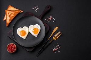 Two heart-shaped fried eggs on a black ceramic plate on a dark concrete background photo