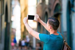 Caucasian tourist with smartphone in hands walking along the narrow italian streets in Rome. Young urban boy on vacation exploring european city photo