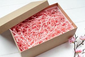 Shredded pink paper packing material texture in a craft box with sakura branch, mockup design photo