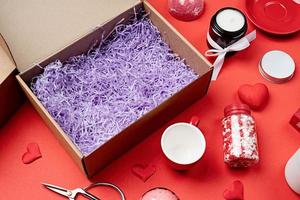 Seasonal gift box for valentine day with candle, red cup and heart shape sweets on red background