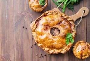 Homemade meat pie with greenery on wooden background photo