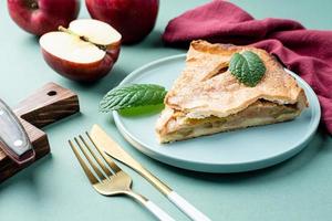 Homemade piece of apple pie with fresh red apples on green table photo