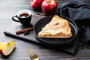 trozo casero de tarta de manzana con manzanas rojas frescas sobre mesa negra foto