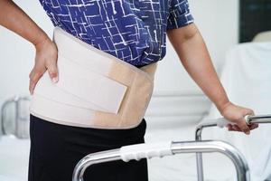 senior asiático dolor de espalda usando cinturón de soporte elástico con andador. foto