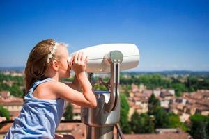 Beautiful little girl looking at coin operated binocular on terrace at small town in Tuscany, Italy photo