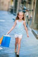 retrato de una adorable niña caminando con bolsas de compras al aire libre en una ciudad europea. niño pequeño de moda en la ciudad italiana con sus compras foto