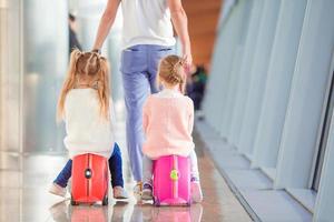 Adorable little girls in airport sitting on suitcase waiting for boarding photo