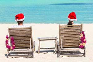 pareja joven con sombreros de santa relajándose en la playa tropical durante las vacaciones de navidad foto