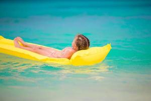 Adorable little girl relaxing on matrasses on white beach photo