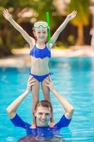 Little girl and happy dad having fun together in outdoors swimming pool photo