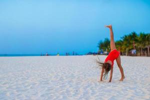 Adorable little girl having fun making cartwheel on tropical beach at sunset photo